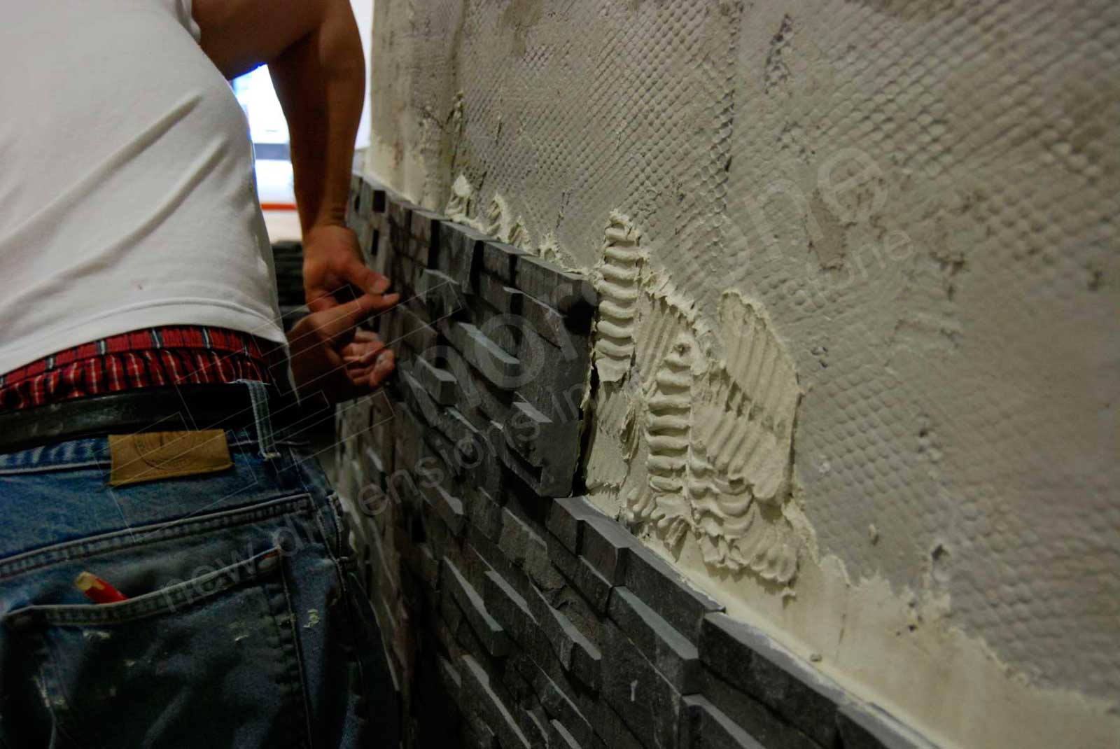 Closeup of man setting a Norstone stone veneer panel in place on cement board using modified thinset